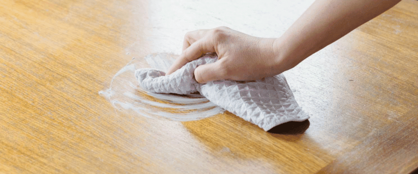 Hand wiping a wooden surface with a cloth to clean and remove dirt or stains.