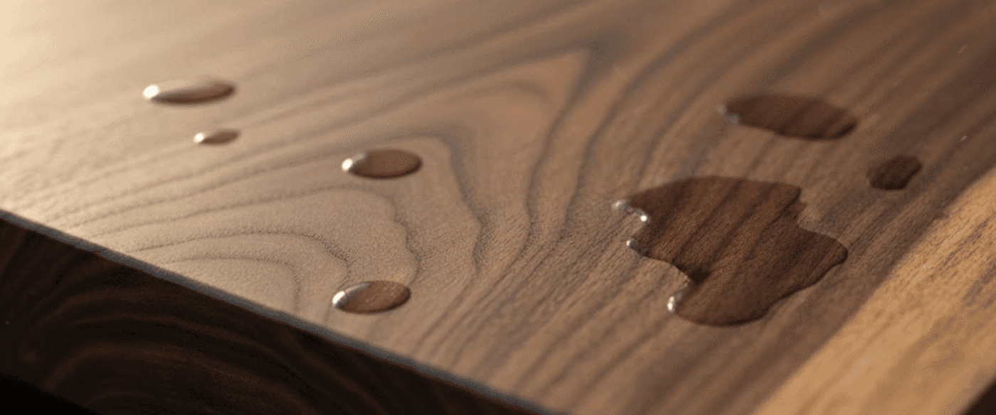 Polished walnut tabletop with natural grain and scattered water droplets catching soft warm light, close-up on the table edge