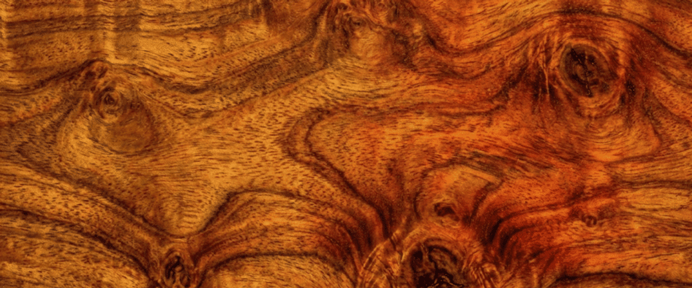 Warm, richly grained wood surface with swirling knots and amber-brown tones, showcasing natural texture and organic patterns across the plank