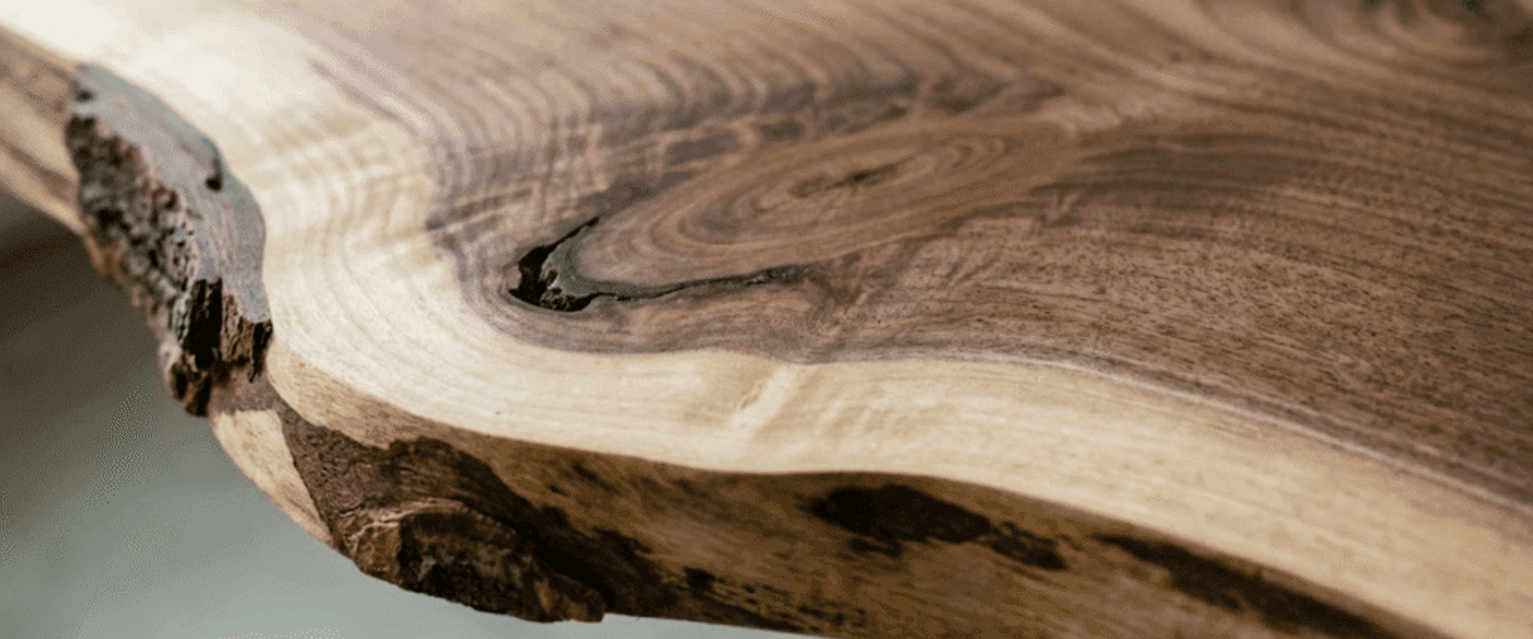 Polished live-edge walnut tabletop showing rich grain patterns, knots, and natural bark edge in warm brown and cream tones