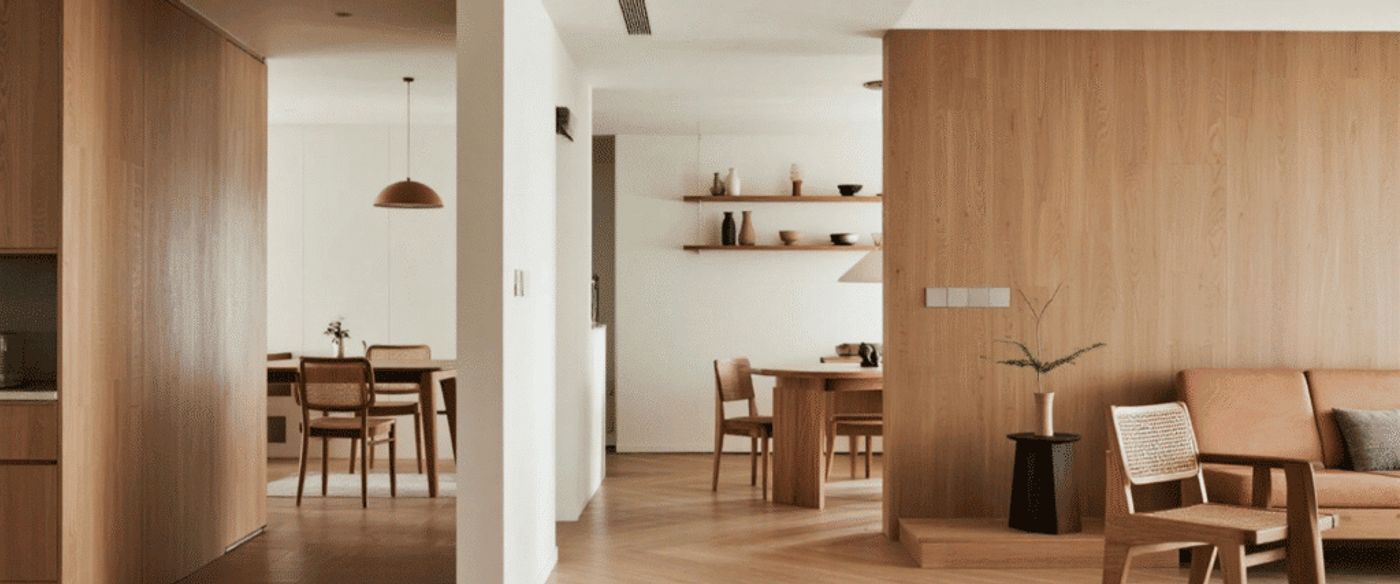 Warm minimalist living and dining area with wooden walls, rattan chairs, leather sofa, and open shelving