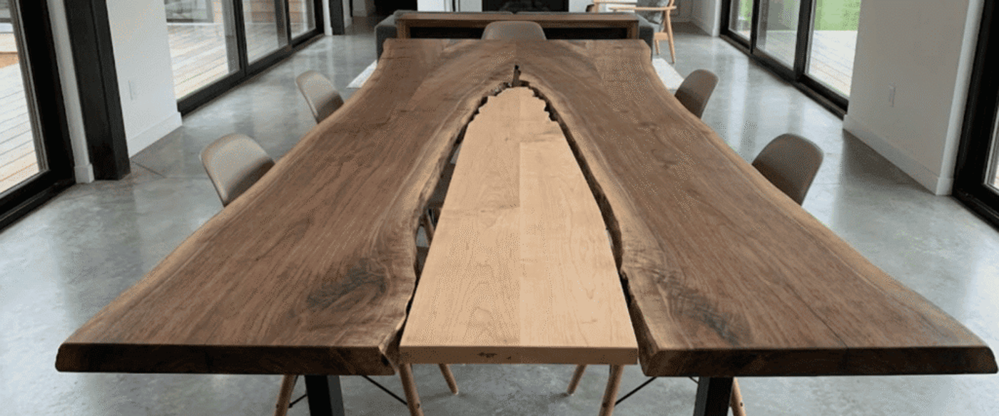 Live-edge walnut dining table with a lighter center inlay, surrounded by chairs in a bright modern glass-walled room