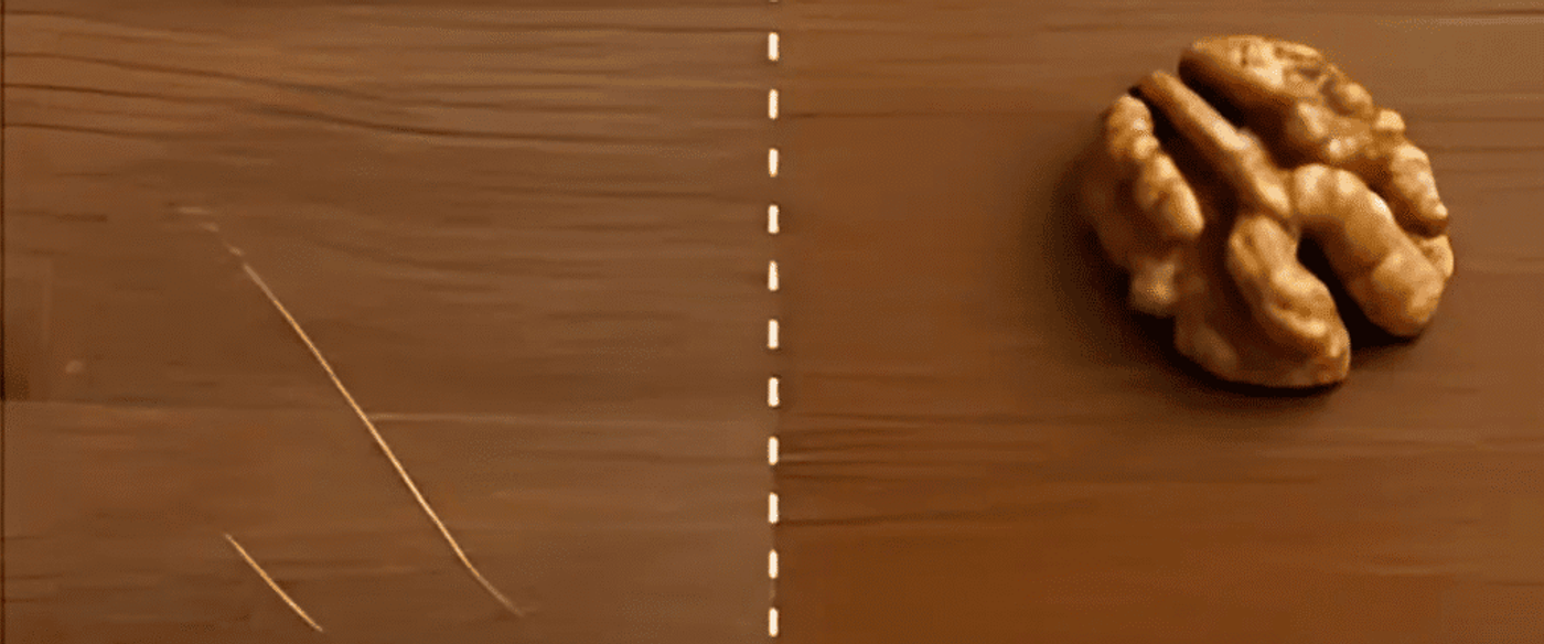 Close-up of a wooden surface showing scratches on the left side and a whole walnut on the right side, separated by a dashed white line