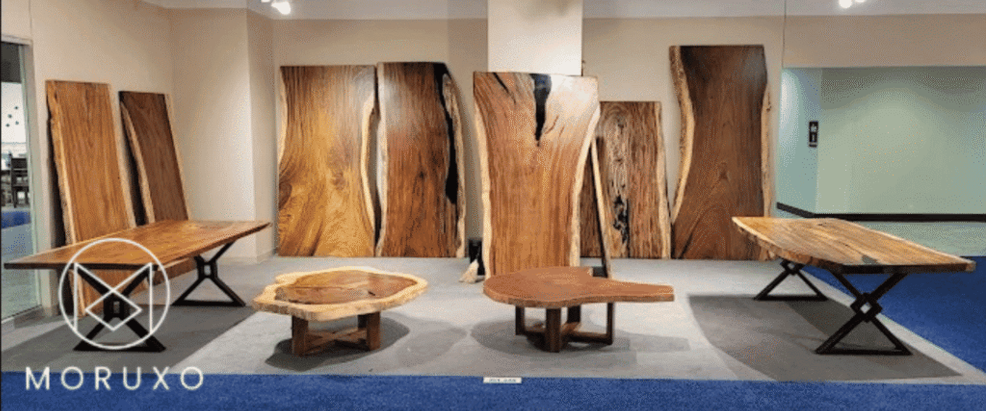 Live-edge wooden slabs and tables on display: three slab-top tables with metal legs and several large natural-edge wood panels standing against a wall.