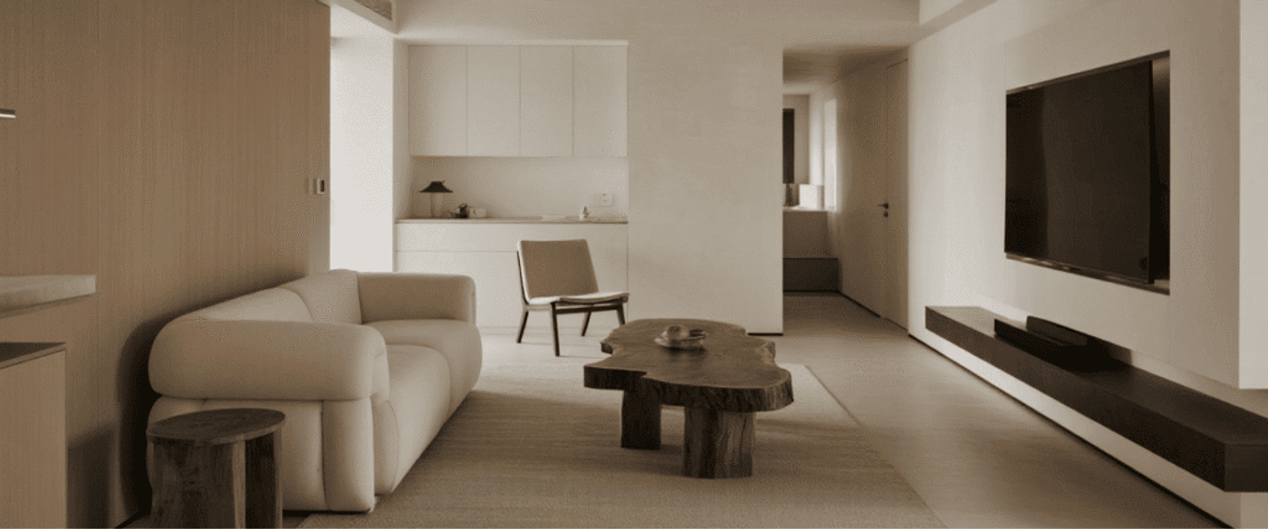 Modern minimalist living room with neutral tones, featuring a cozy sofa, wooden coffee table, wall-mounted TV, and simple decor.