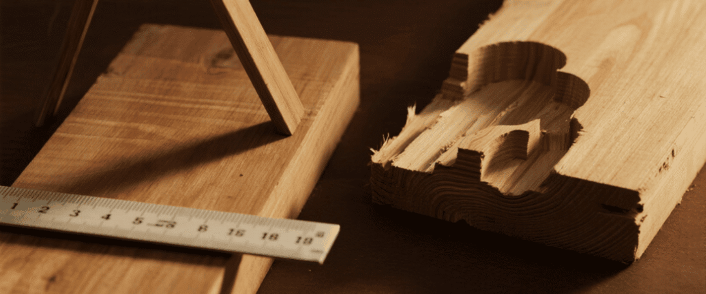 Wood plank with a carved groove, a metal ruler and a wooden support on a dark workbench, close-up of woodworking tools and grain.
