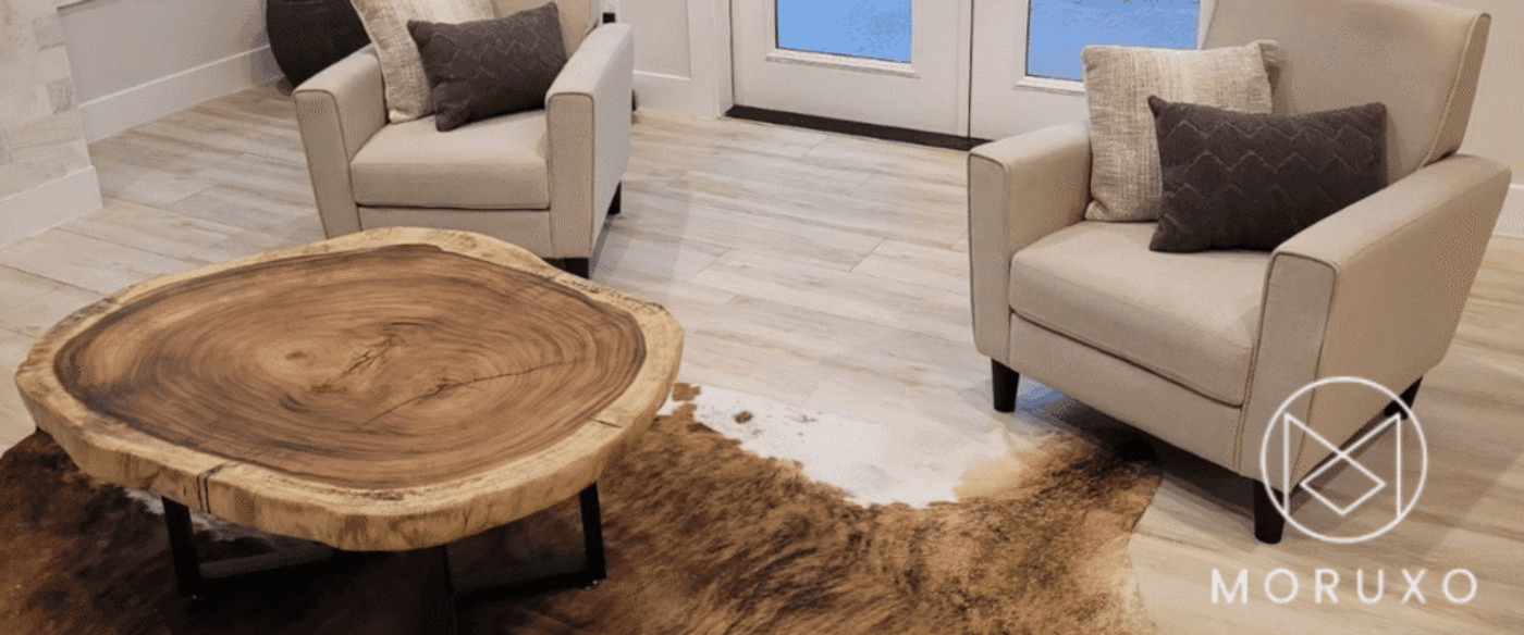 Modern living room with two beige armchairs, textured throw pillows, a live-edge wood coffee table on a brown cowhide rug.
