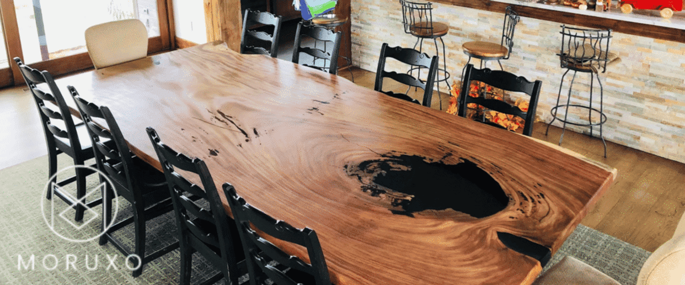 Live-edge walnut dining table with black resin center in a rustic kitchen featuring wooden cabinets and bar stools