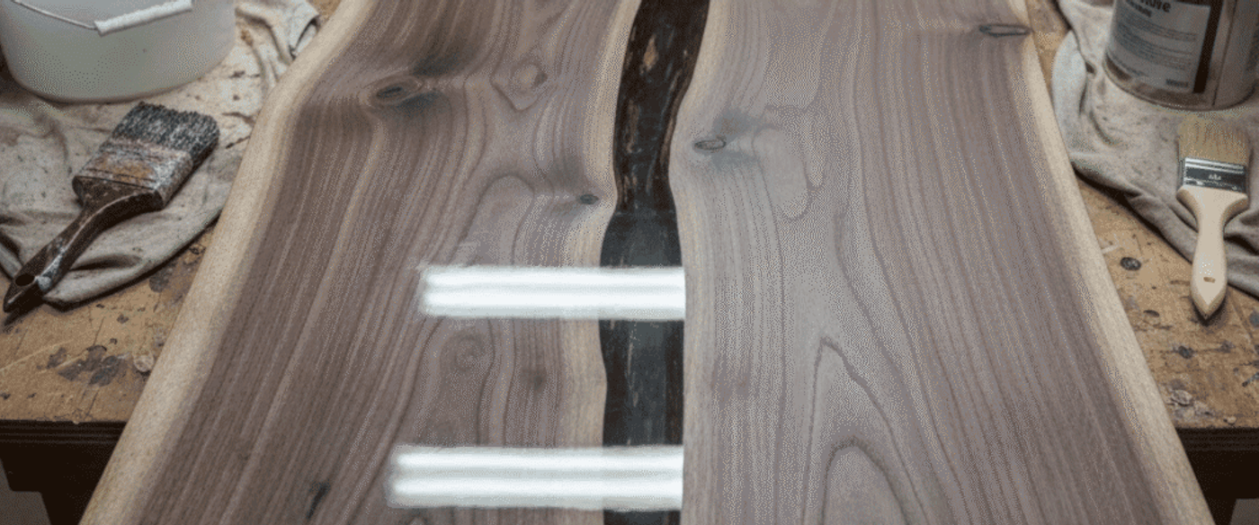 Walnut live-edge table with a dark resin-filled center crack on a workshop bench surrounded by brushes and cans