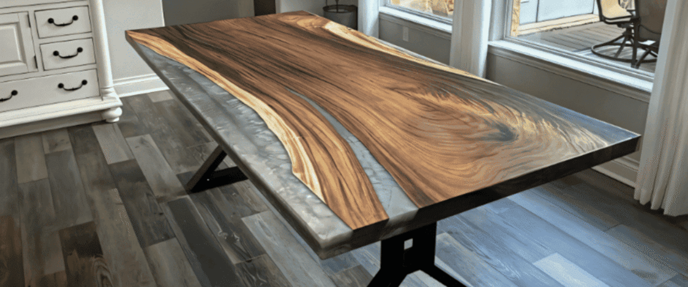 Live-edge wood and resin dining table with black metal legs under a chandelier in a bright dining room by large windows