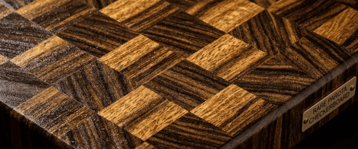 Polished checkerboard-style wooden cutting board with alternating dark and light Parota wood squares and engraved brass label