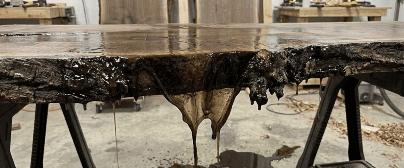 Live-edge walnut slab on sawhorses with glossy epoxy finish dripping down bark edge onto workshop floor