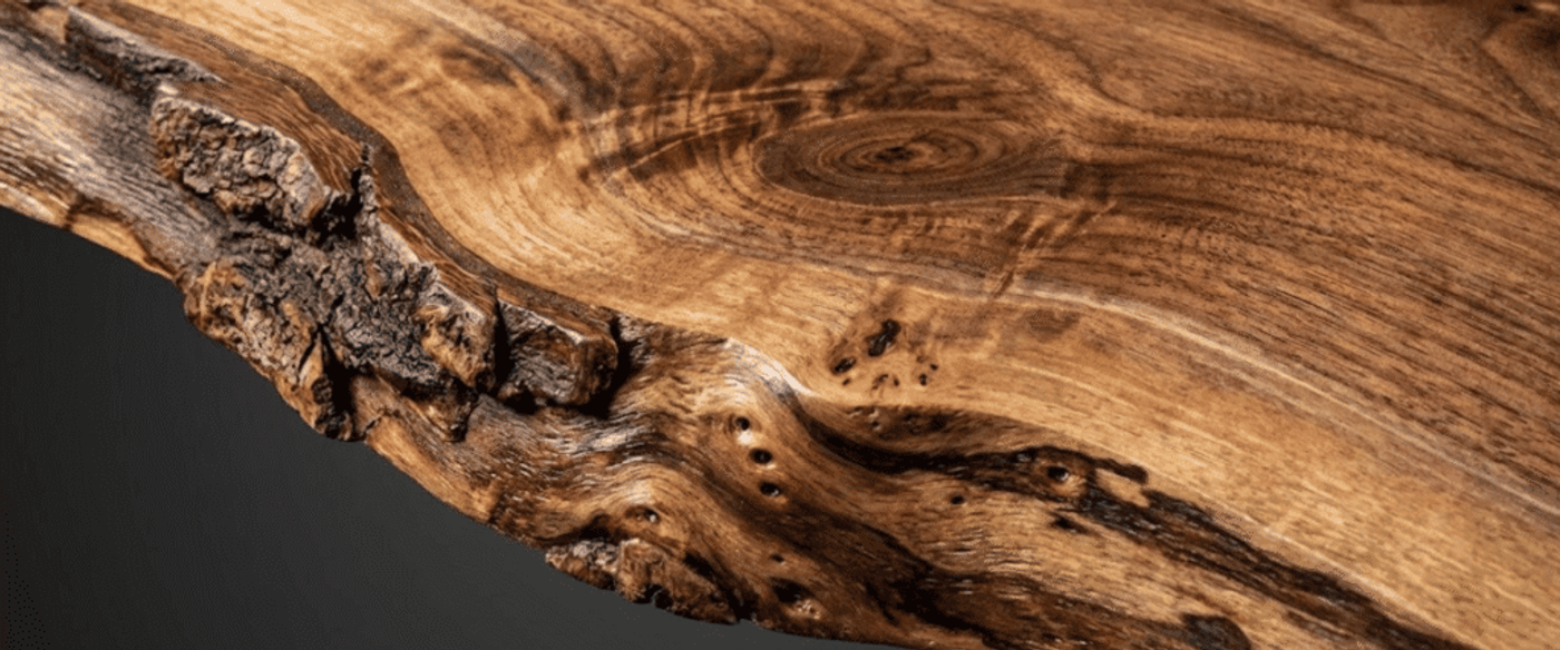 Live-edge walnut slab with rich grain, knots, and textured bark along the natural, polished edge for woodworking or table top
