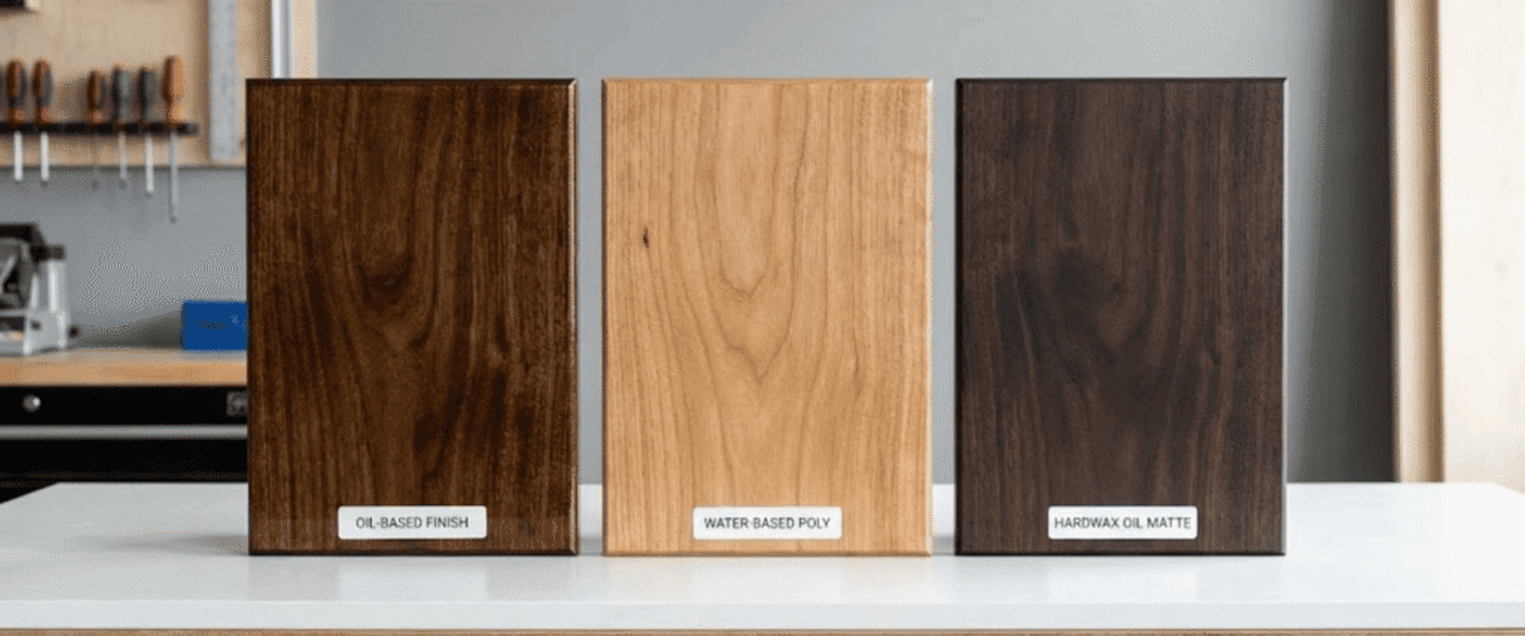 Three wood sample panels on a bench labeled Oil-based finish, Water-based poly, and Hardwax oil matte, showing finish differences