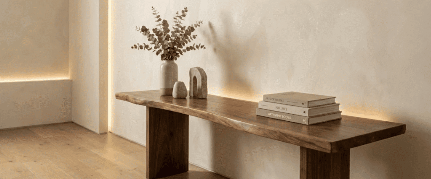 Minimal wooden console table against a cream wall with a vase of dried branches, sculptural decor, and stacked books, warm LED backlight