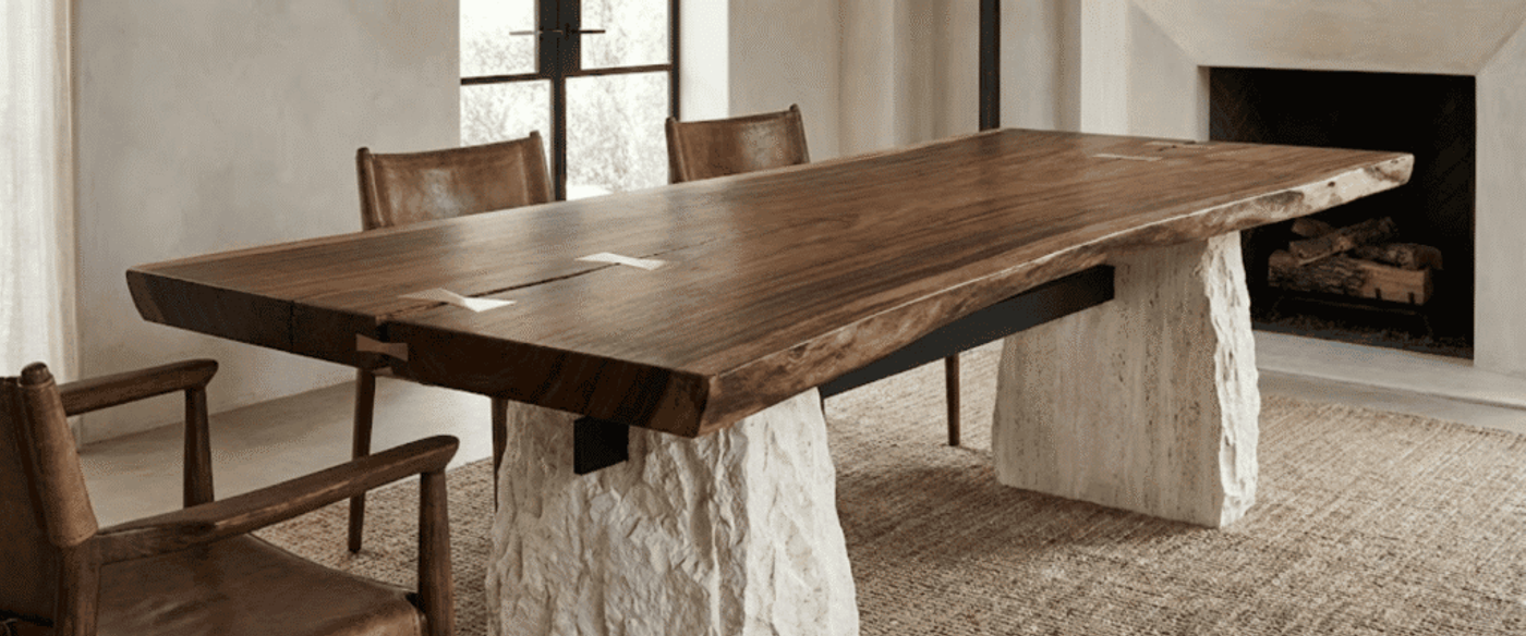 Rustic live-edge walnut dining table with stone pedestal legs, leather chairs, woven rug and fireplace in a sunlit modern dining room