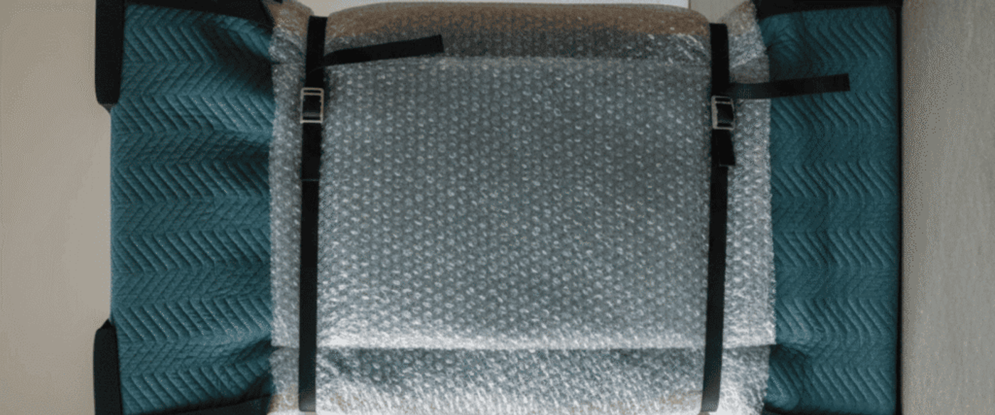 Wrapped teal armchair standing upright, covered in bubble wrap and moving blankets secured with two black straps
