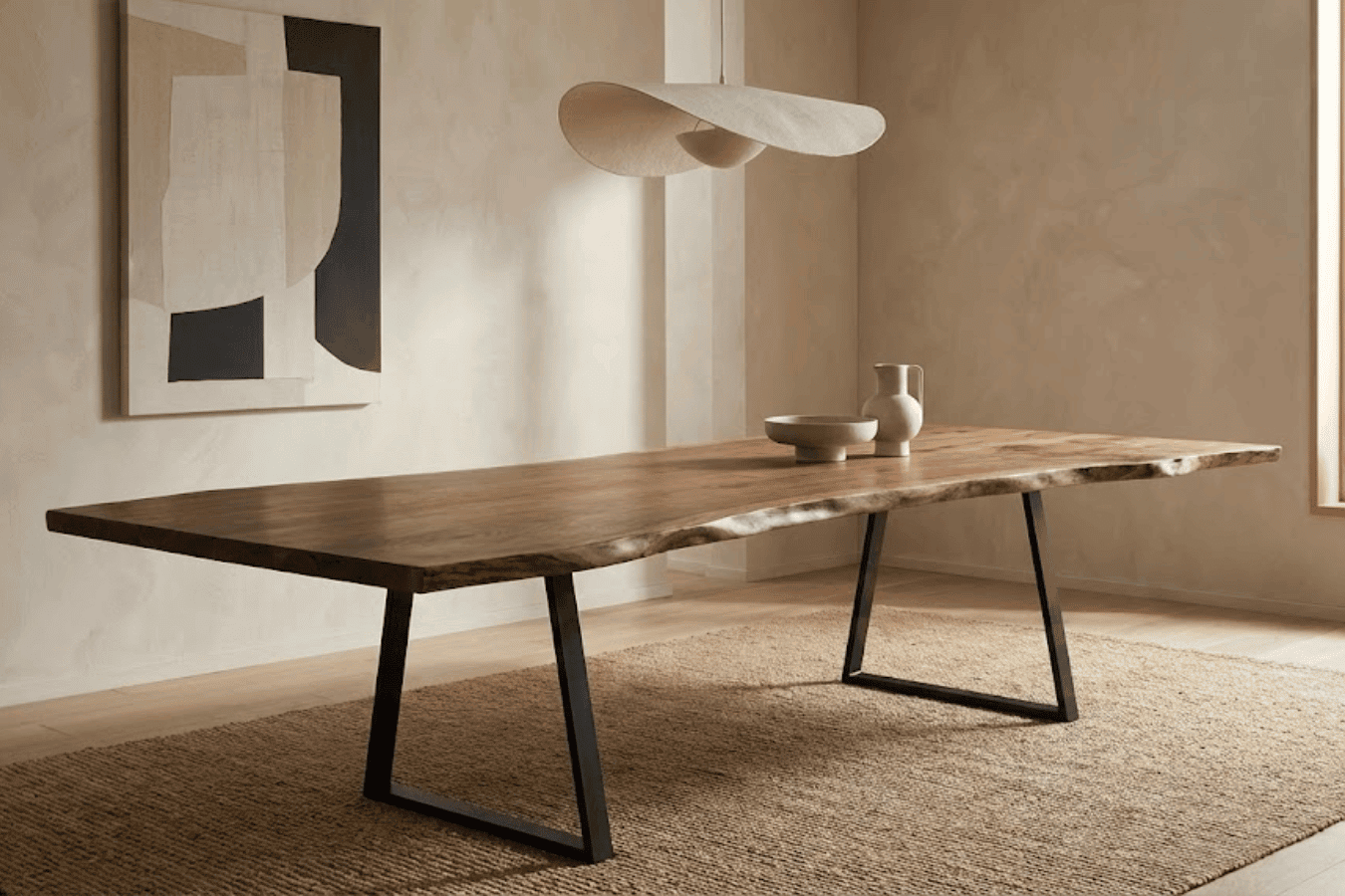 Live-edge wooden dining table with black metal legs in a minimalist beige room, decorative ceramics, abstract wall art, and natural light