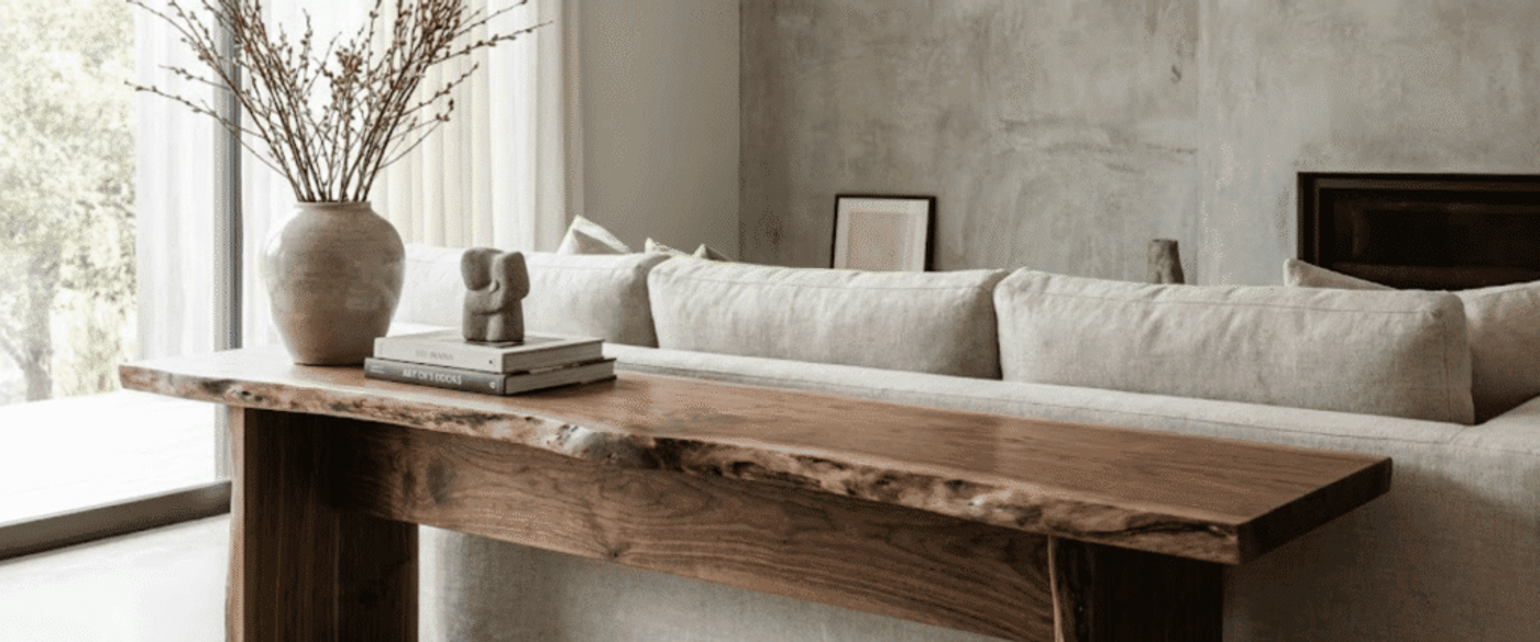 Neutral-toned living room with a wooden console behind a beige sofa, vase with branches and stacked books on the table