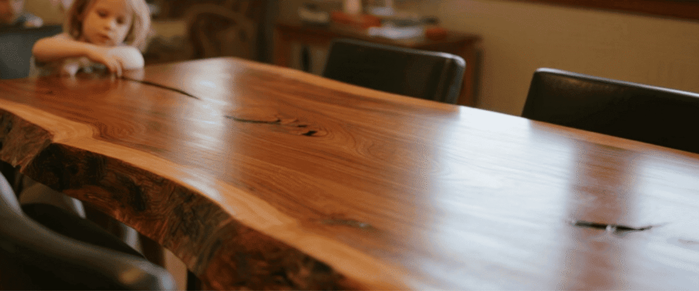Polished live-edge wooden dining table with leather chairs in a cozy sunlit living room, children playing in the background.