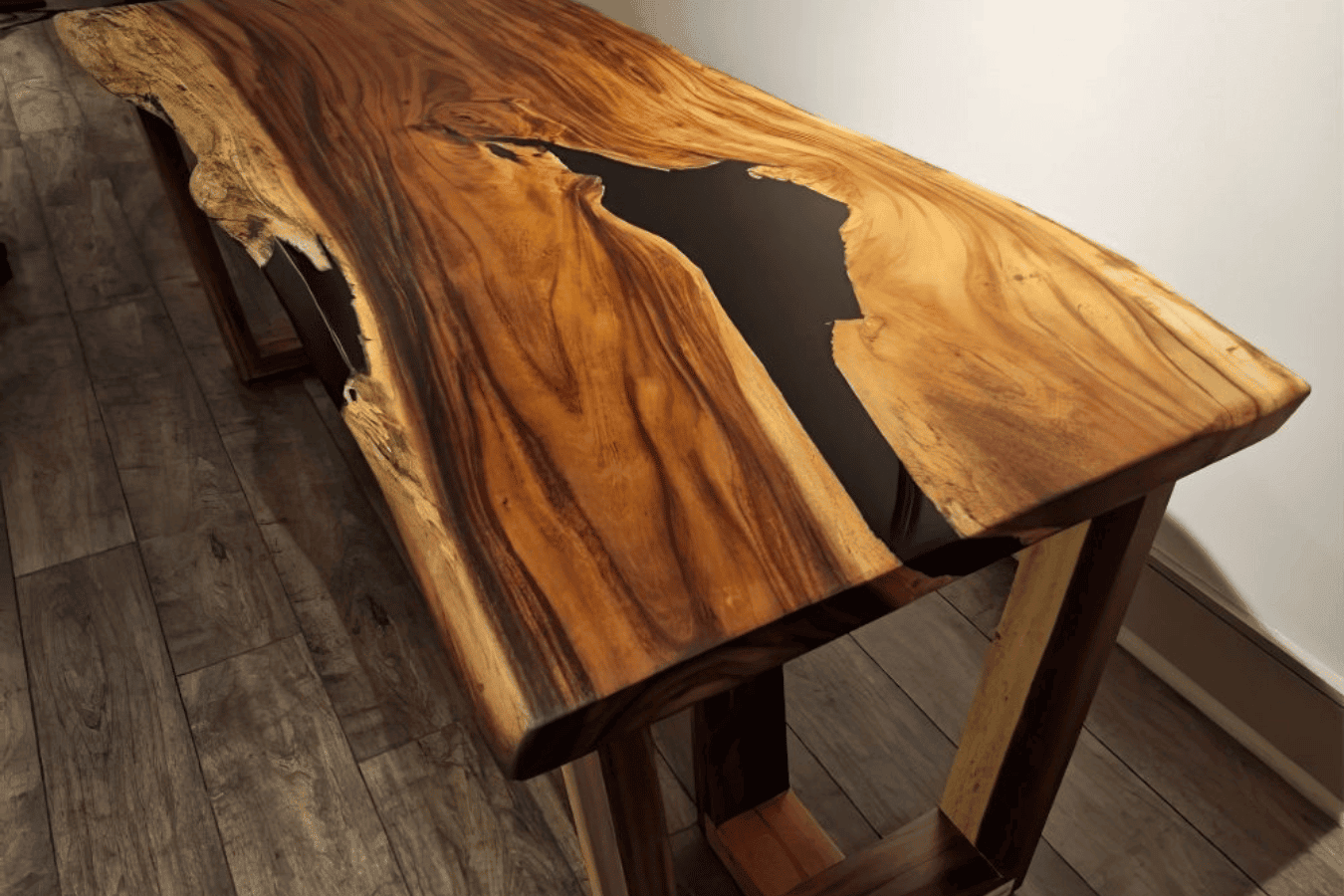 Live-edge walnut table with a black epoxy river running through its natural grain, standing on wooden trestle legs.