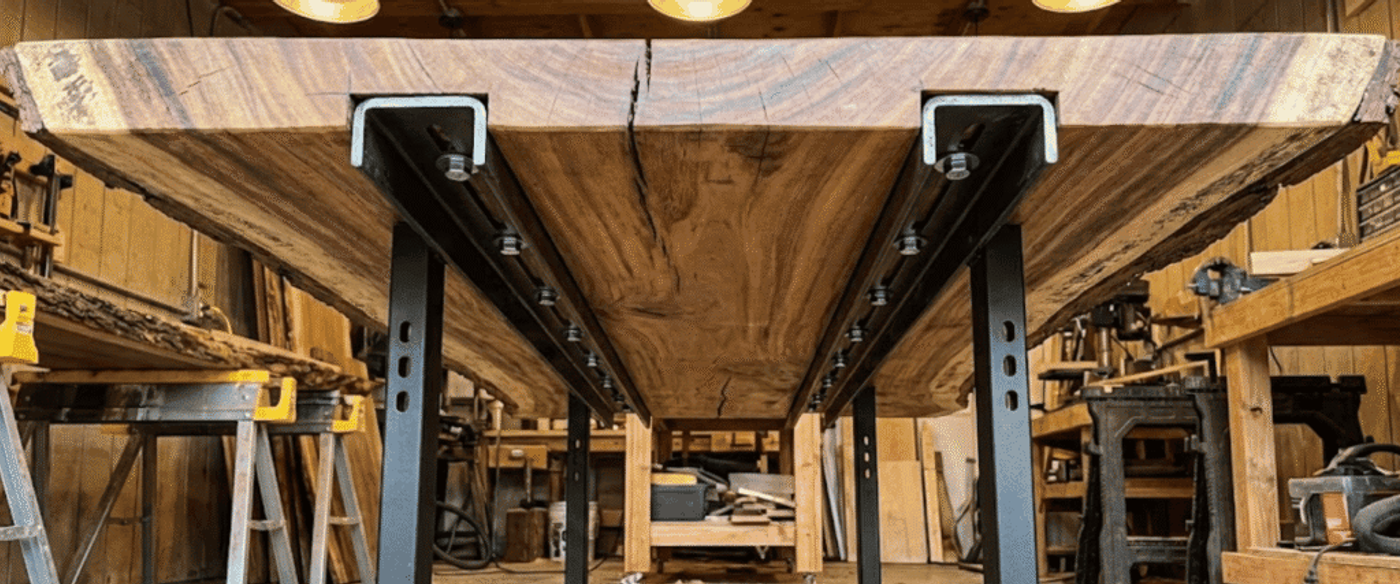 Live-edge walnut slab dining table with black metal legs in a woodshop