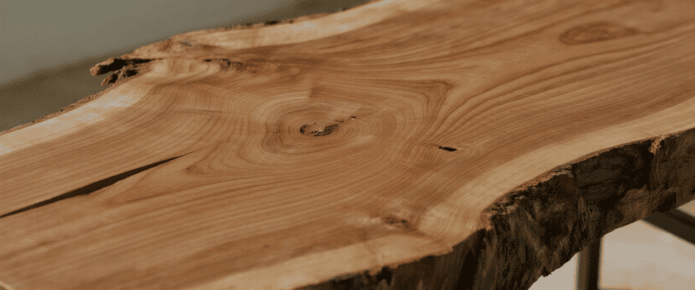 Live-edge wooden slab table with rich grain, growth rings, knots, and natural bark edge mounted on metal legs.