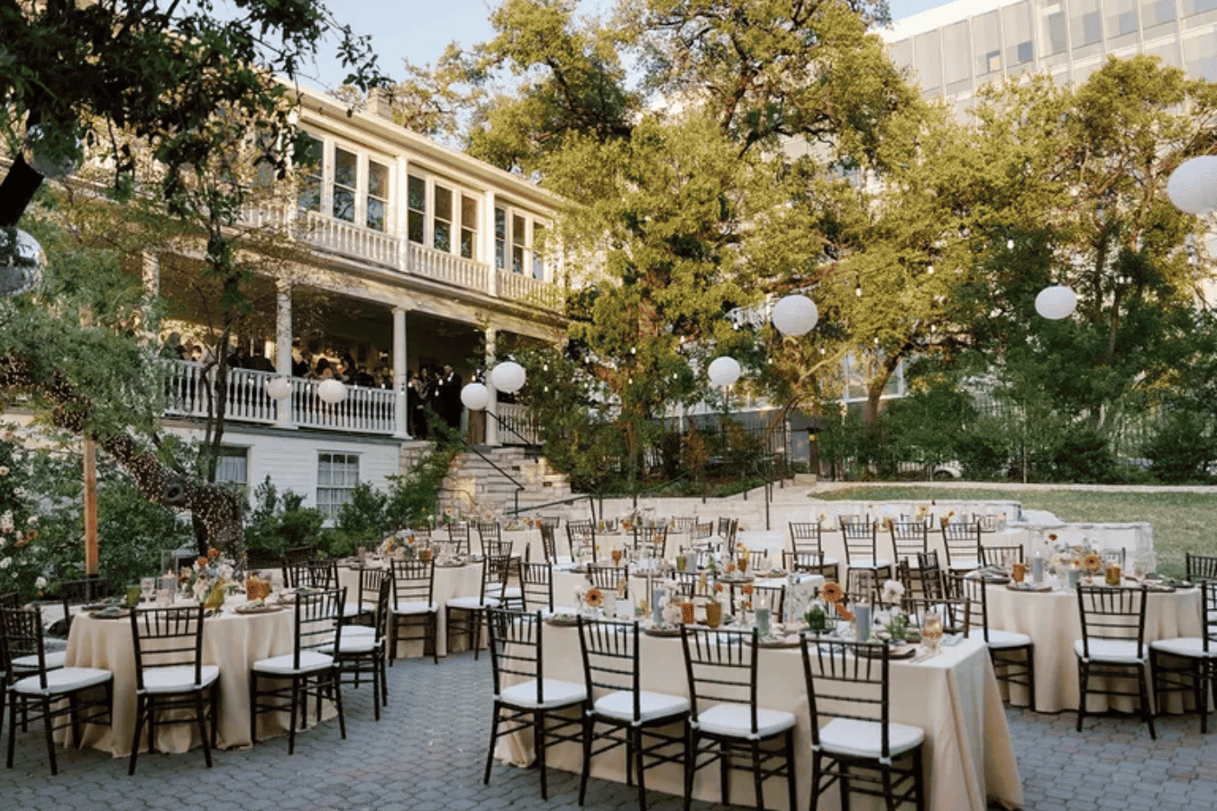 Outdoor wedding reception courtyard with gold chairs, round tables, historic building backdrop, and mature trees