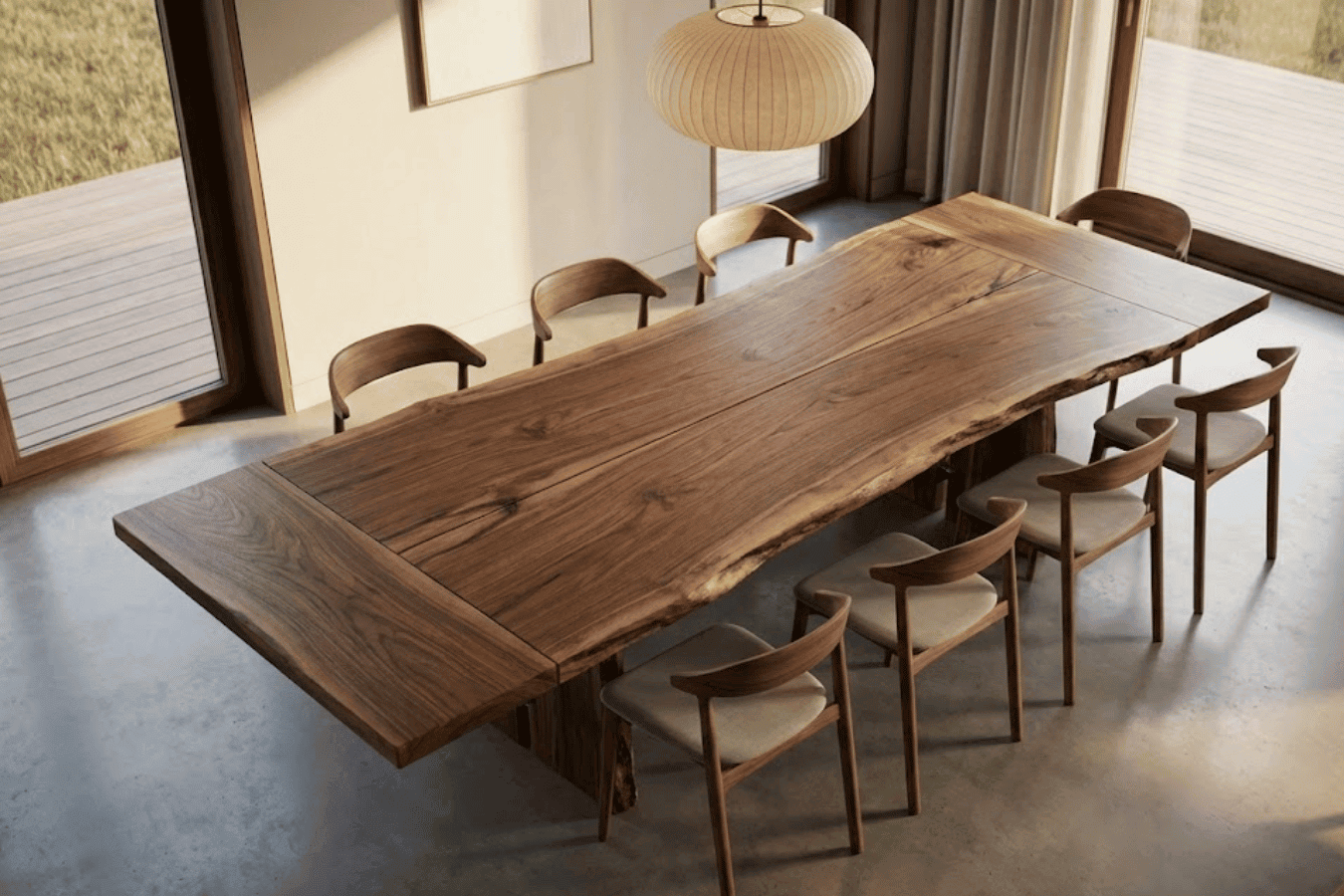 Long live-edge walnut dining table with eight wooden chairs in sunlit modern room, large windows and pendant light overhead