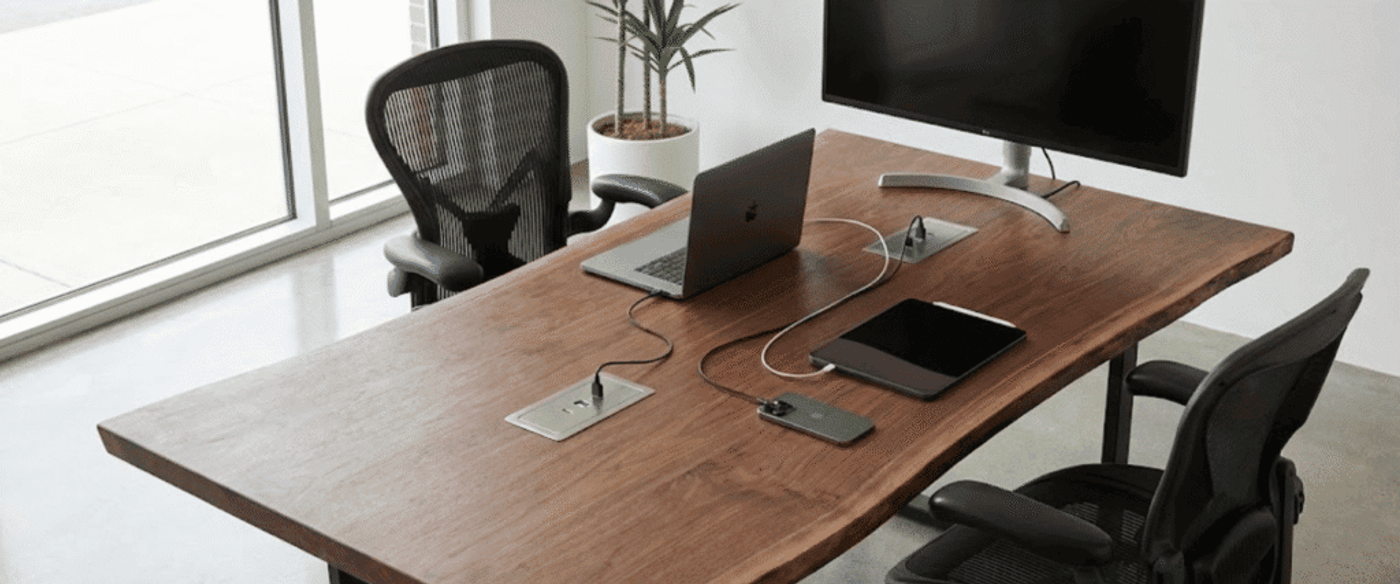 Clean modern office desk with live-edge wood top, two mesh ergonomic chairs, laptop, tablet, smartphone and monitor by window