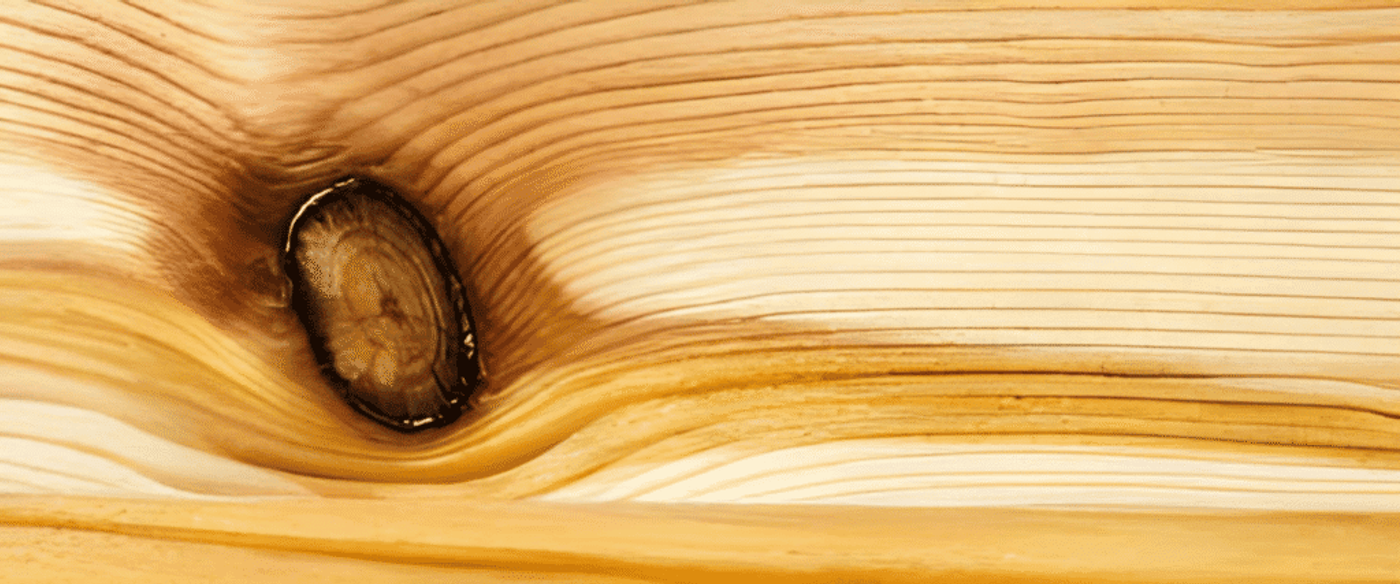 Wood grain close-up with a knot and flowing growth rings in warm golden tones.