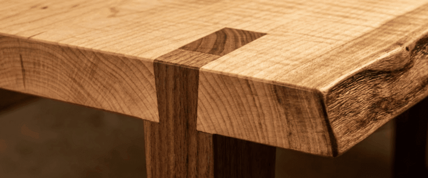 Live-edge wooden table corner with dovetail joint, contrasting grain and smooth finish highlighting natural texture and craftsmanship
