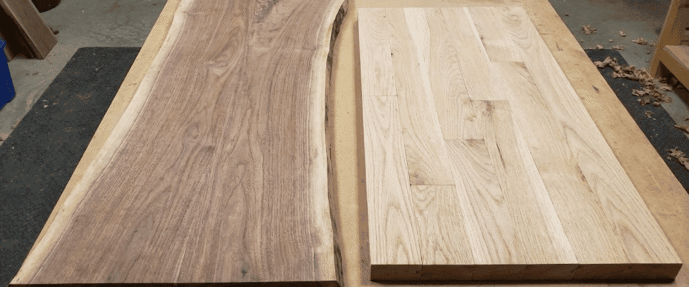 Raw and finished wood slabs on a workbench: a natural-edge walnut slab beside a glued-up oak panel with hand tools and shavings