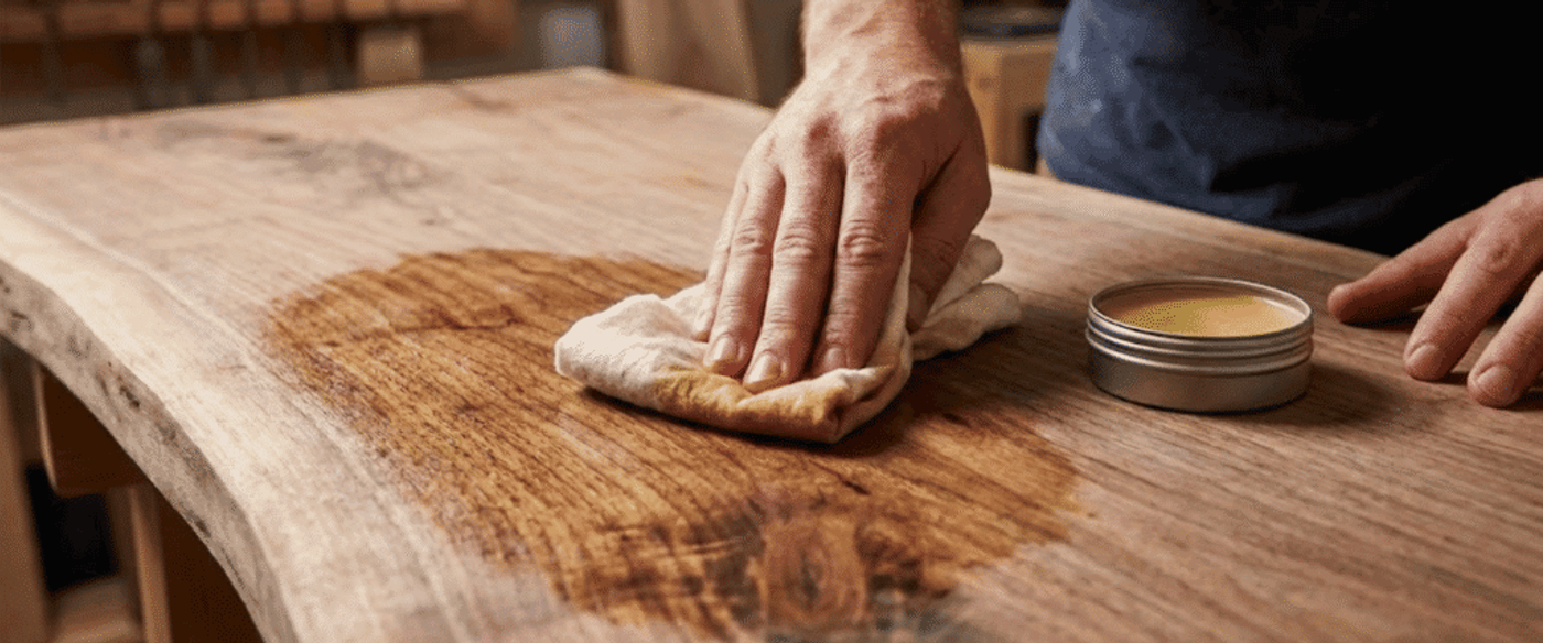 Hand rubbing wood conditioner onto a live-edge tabletop with a cloth, restoring grain and sheen
