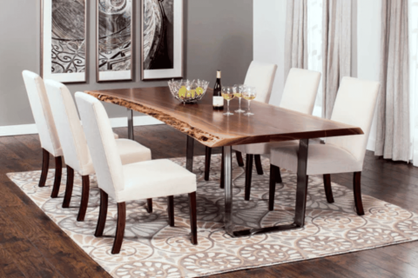 Live dining room with a live-edge wooden table, eight white upholstered chairs, patterned rug and modern wall art.