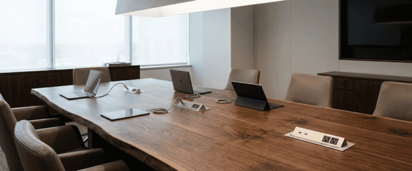Modern conference room with a long wooden table, leather chairs, laptops and tablets, power outlets, and large windows with city view
