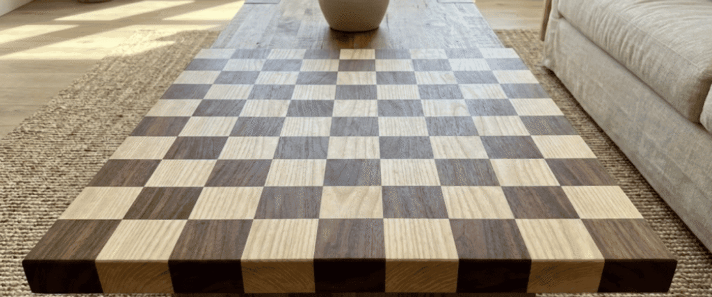 Handcrafted wooden checkerboard coffee table with alternating light and dark squares, vase centerpiece, sofa and woven rug in bright living room