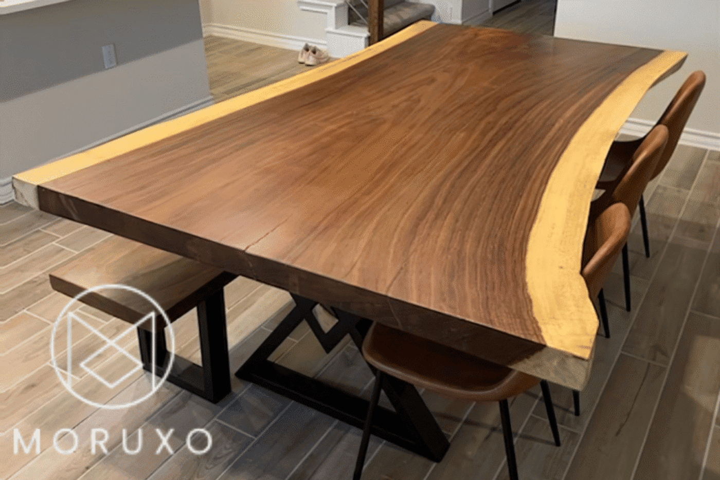 Live edge wooden dining table with metal legs and brown chairs, showing natural wood grain and irregular edges.