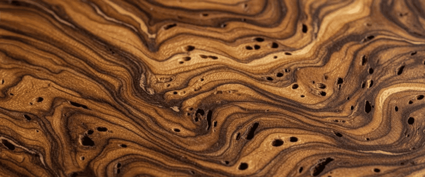 swirled brown wood grain with flowing lines and small irregular holes, showing natural texture and depth