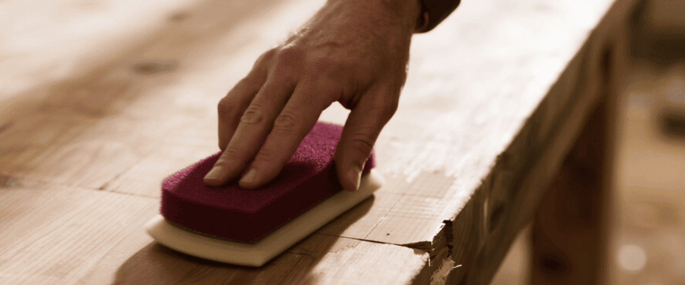 wood area with a maroon buffing pad, blending sheen. Side lighting highlights the transition between repaired and original finish