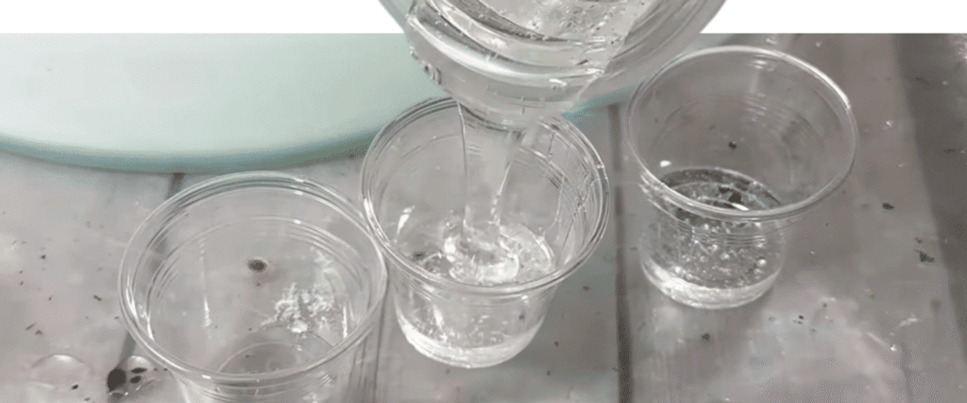 Pouring clear liquid into small transparent plastic cups on a table.