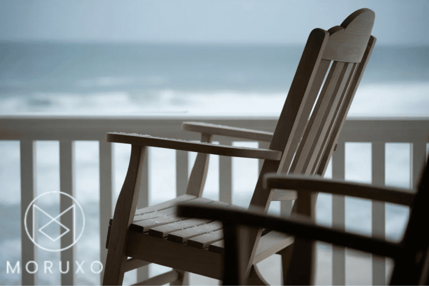 Wooden rocking chair on porch overlooking ocean waves, calm and peaceful setting.
