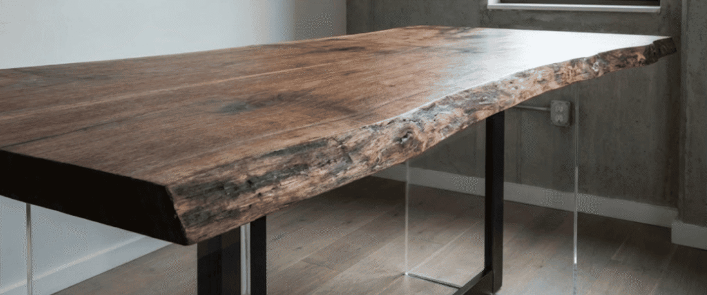 Live-edge walnut tabletop with natural grain and bark edge, mounted on metal and clear acrylic legs in a minimalist room