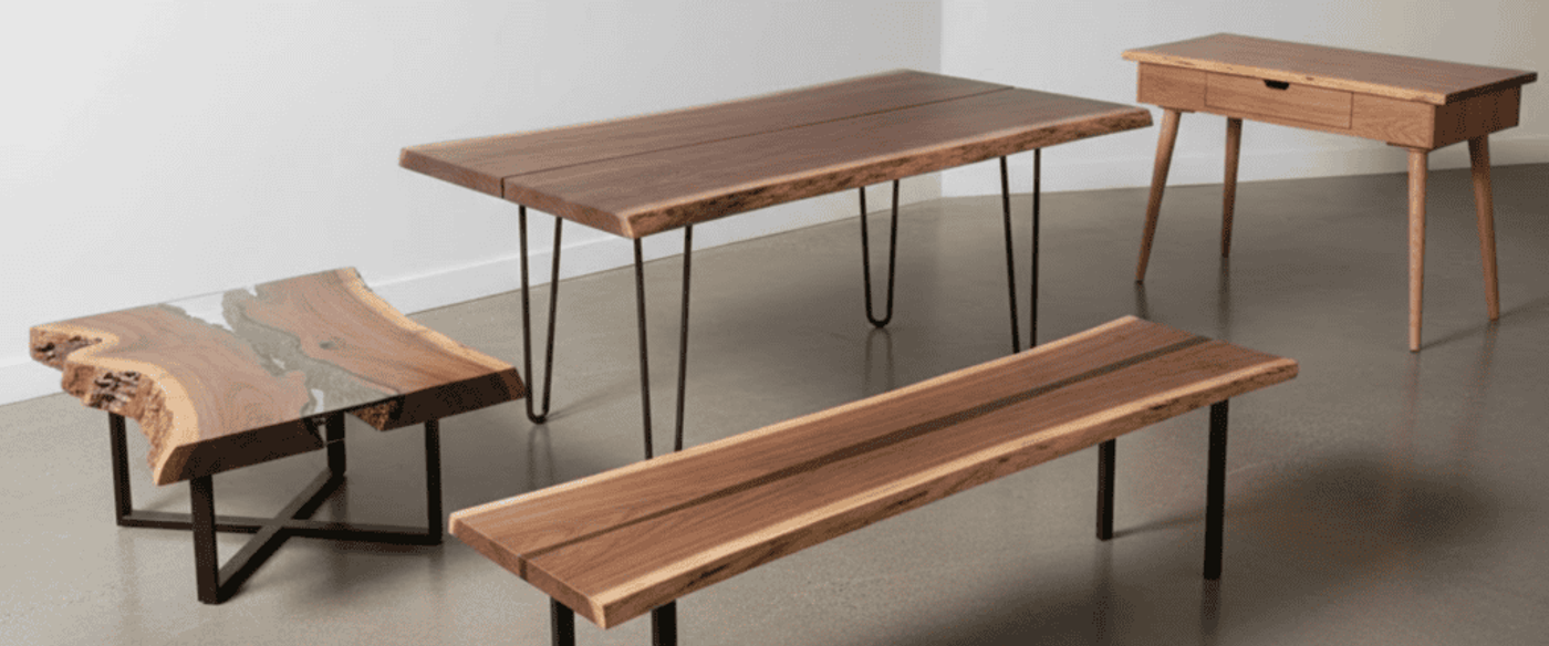 Live-edge wood table, bench, coffee table with resin river and mid-century desk arranged on concrete floor against white walls