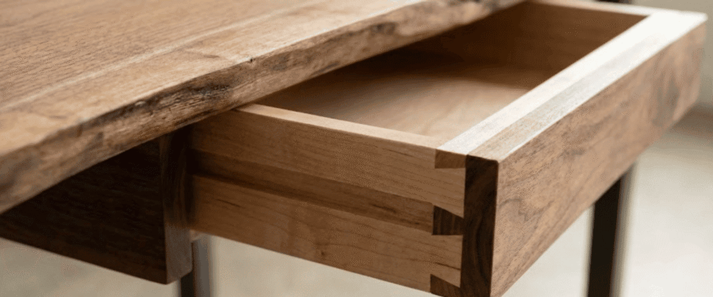 Open drawer of a wooden desk showing dovetail joints and smooth natural grain on a handcrafted maple and walnut drawer