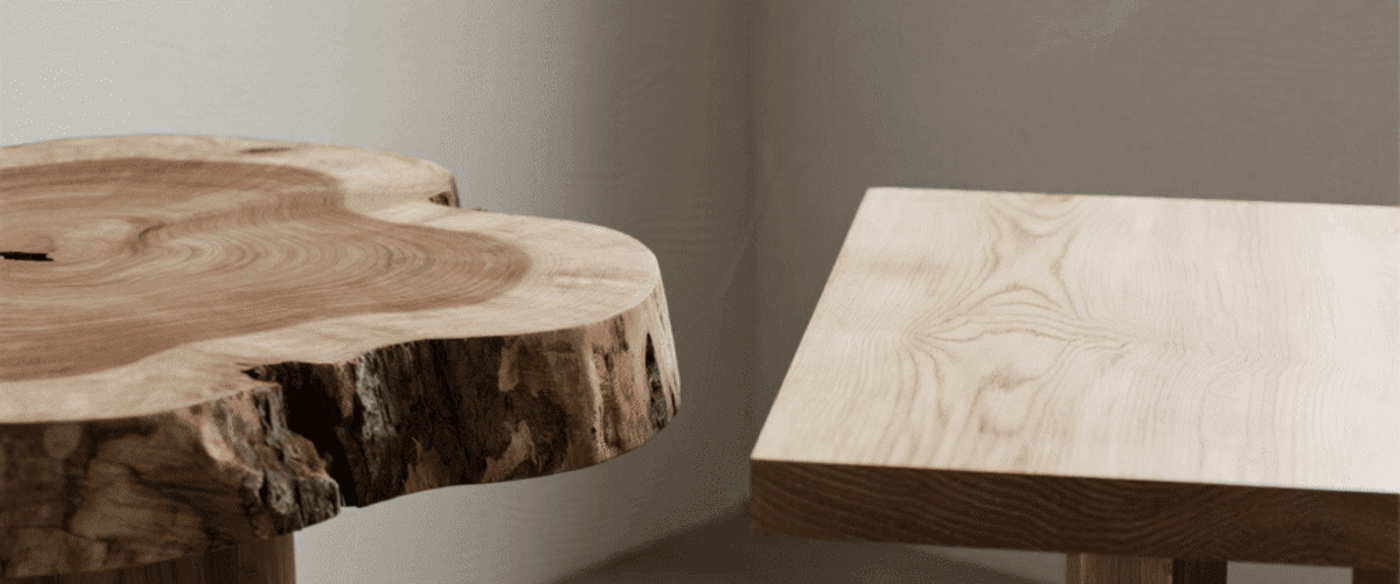 Organic live-edge wood slab table next to a smooth rectangular wooden bench, both showing natural grain and bark textures in soft light.