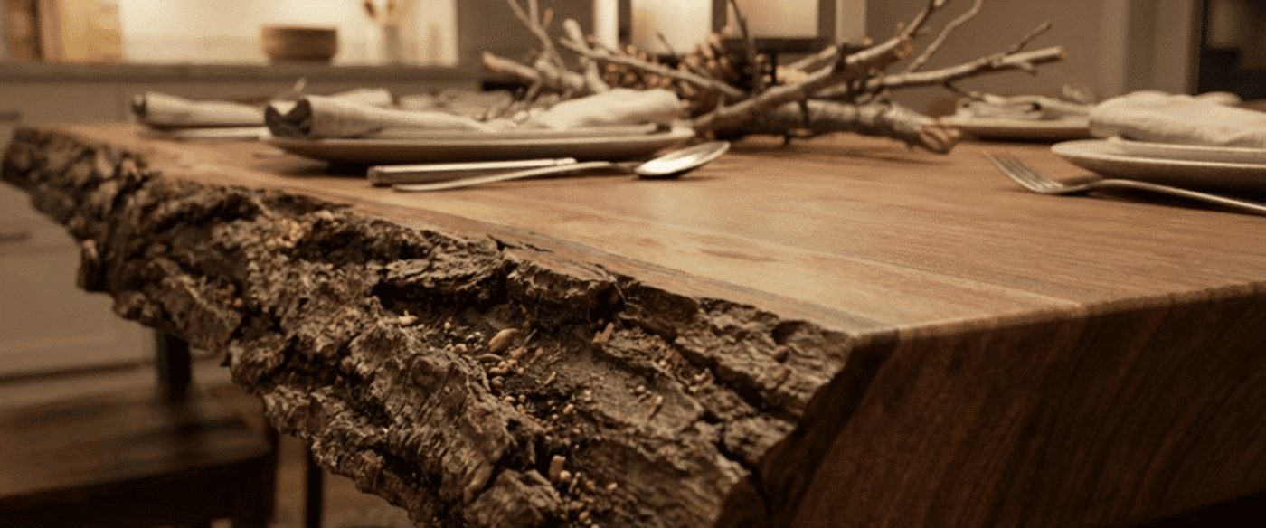Live-edge walnut dining table with natural bark edge, set with plates, cutlery, and rustic twig centerpiece in warm lighting