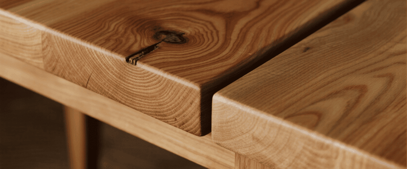 Natural oak bench detail showing smooth grain, rounded edges, knot and crack in plank, warm honey finish on sturdy legs.