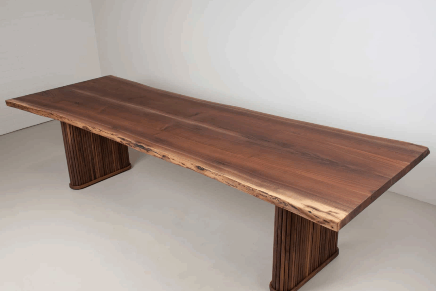 Solid wood dining table with natural live edge and sturdy vertical slat legs, showcasing rich wood grain and craftsmanship.
