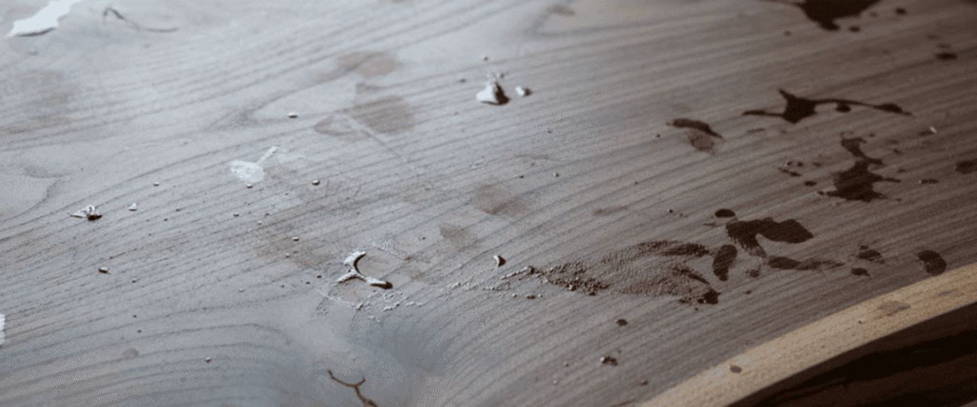 Wooden table with natural grain, live edge and scattered liquid stains and droplets near a sunlit window